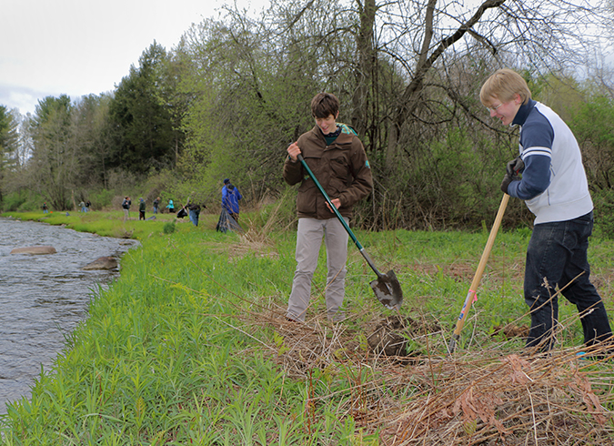 Two students digging along river volunteers in background